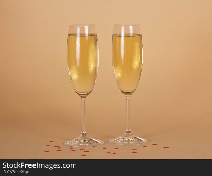 Two wine glasses of champagne and small hearts on a beige background