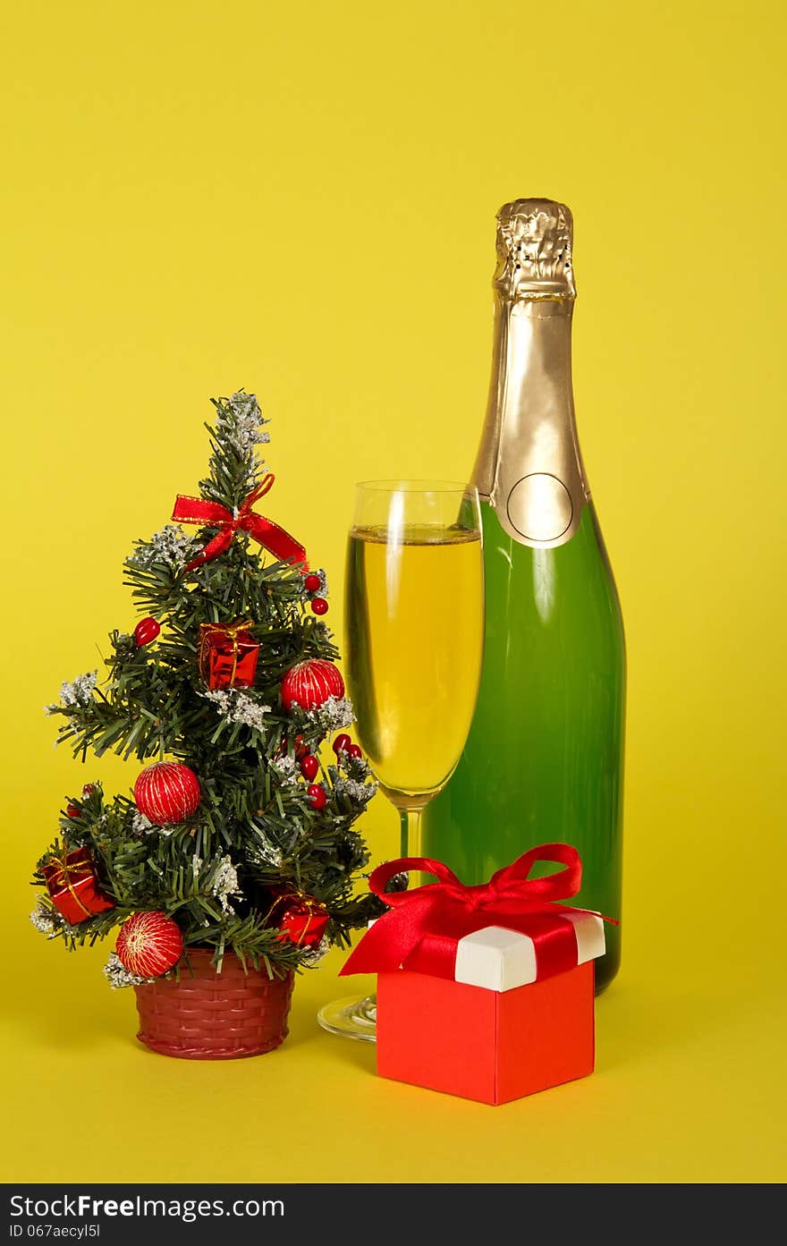 Champagne, small fir-tree in a pot with toys and gifts on a yellow background