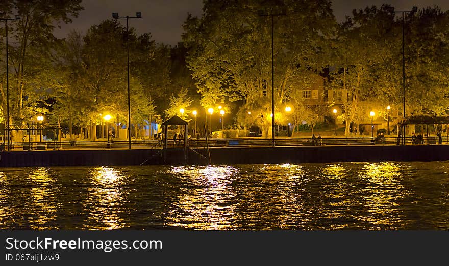 Sidewalk by canal, lit by several lamp posts, and small pier