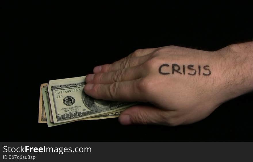 The hand with an inscription crisis takes away dollars from a pack laying on a black background