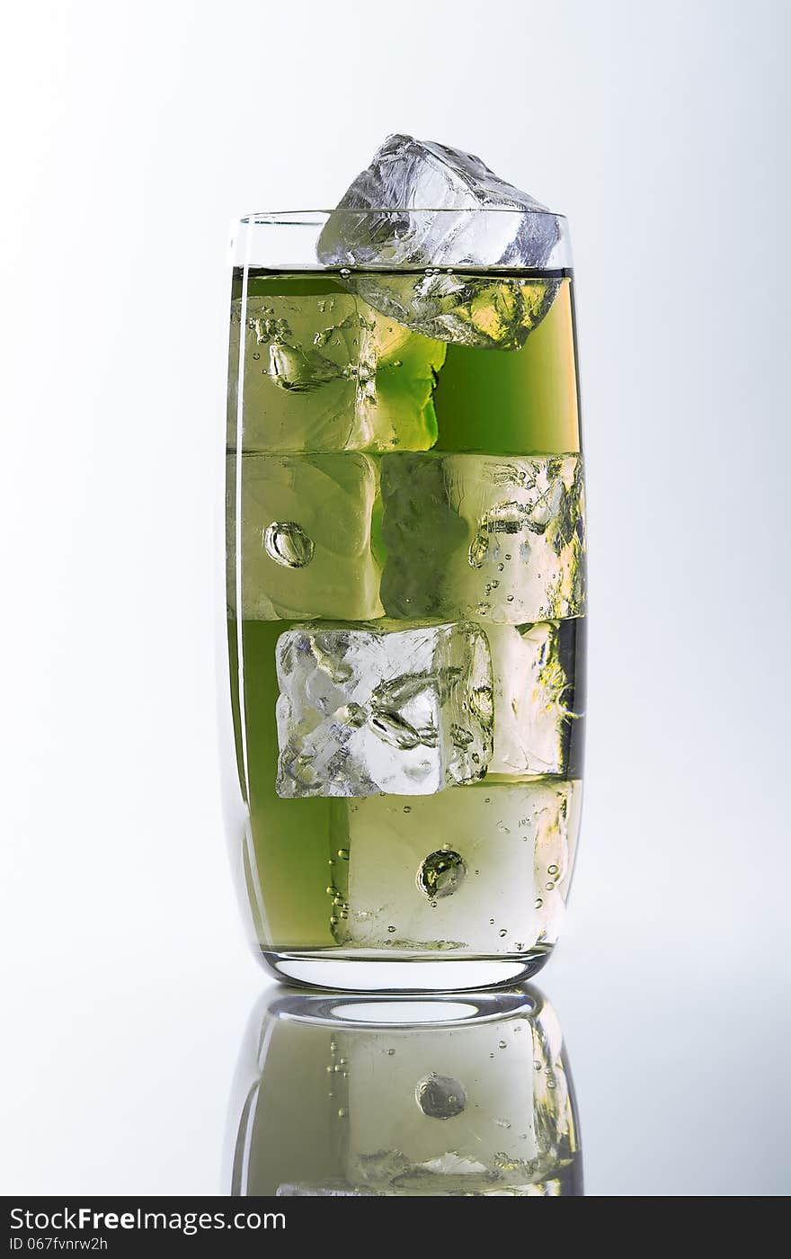 Glass filled with green liquid and ice cubes on a white/grey background (seamless), reflection at the bottom. Glass filled with green liquid and ice cubes on a white/grey background (seamless), reflection at the bottom