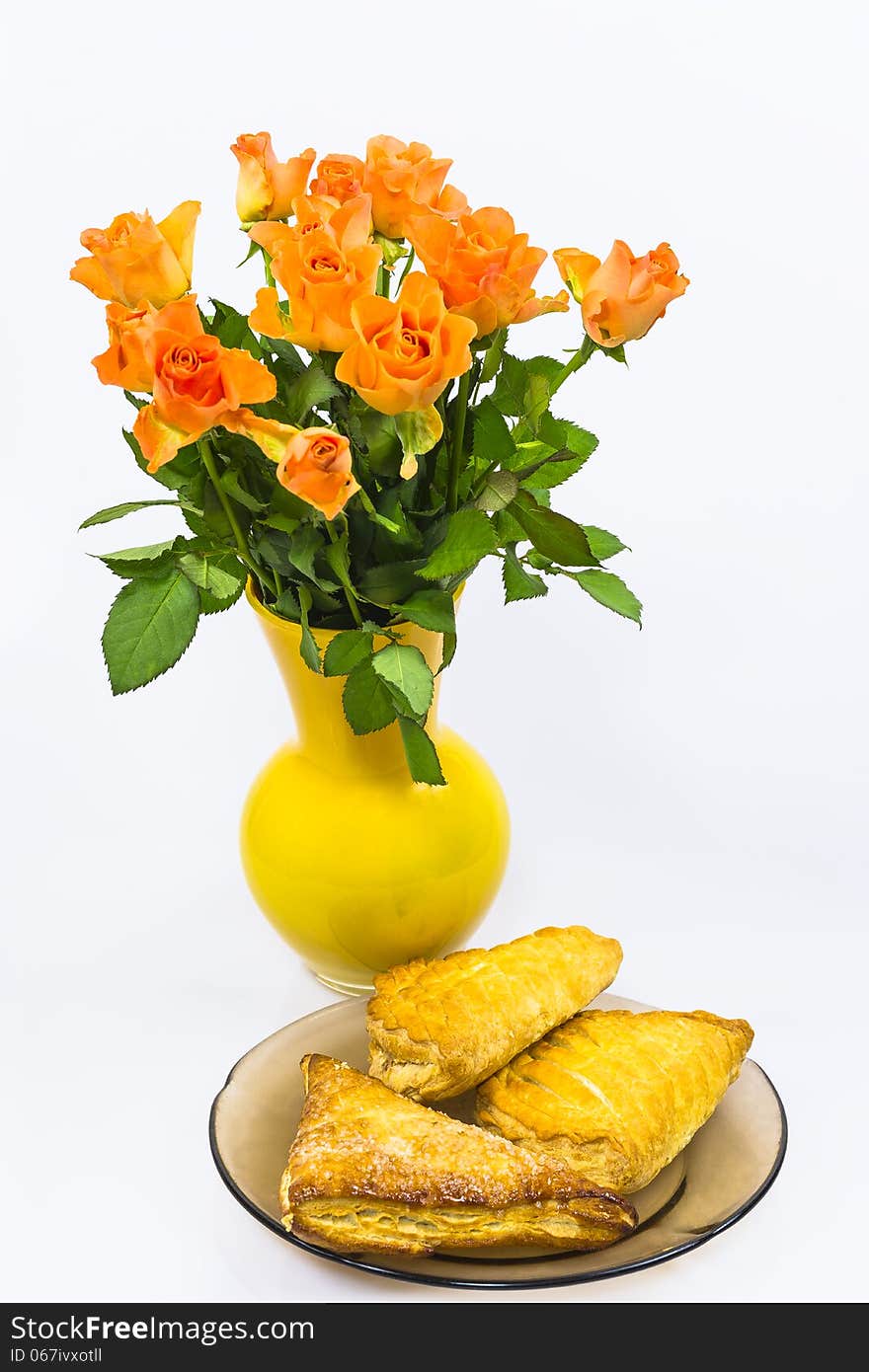 A bouquet of roses in the vase and cakes on a plate. A bouquet of roses in the vase and cakes on a plate