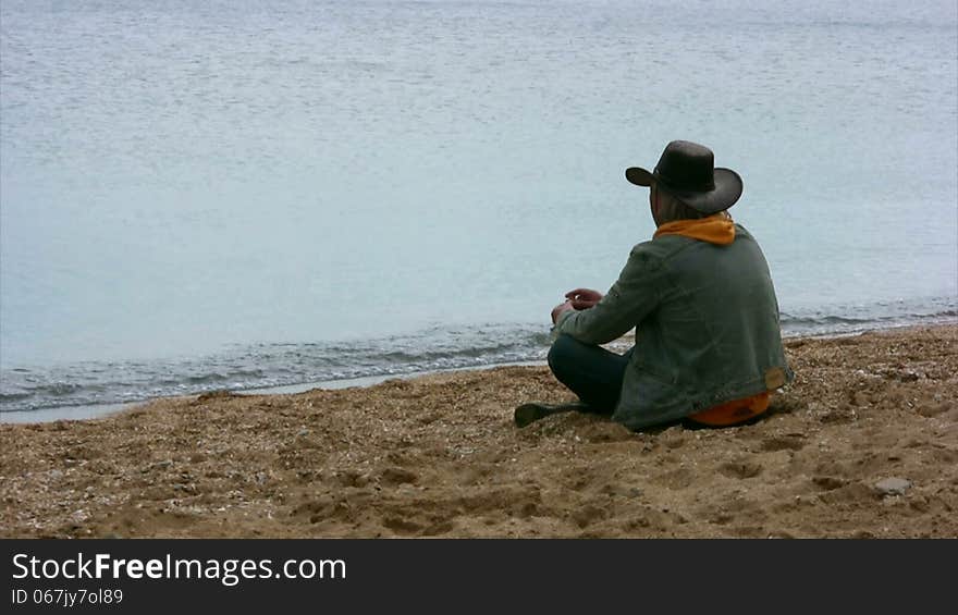 Wistful man sits on a sandy beach and threw stones into the water. Wistful man sits on a sandy beach and threw stones into the water