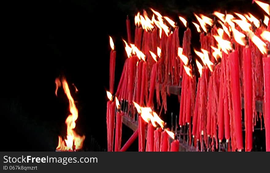 A lot of red ritual candles are burning on a black background. The flames swaying in the wind