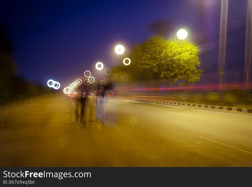 Two persons walking on road with night traffic trails and beautiful colorful bokeh. Two persons walking on road with night traffic trails and beautiful colorful bokeh