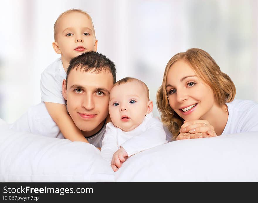 Happy family of father, mother and children in white bed