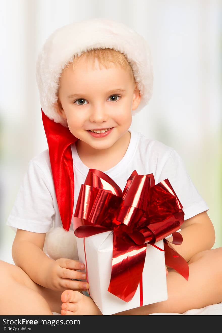 Little cute child boy in a Christmas hat with a gift box with ribbon