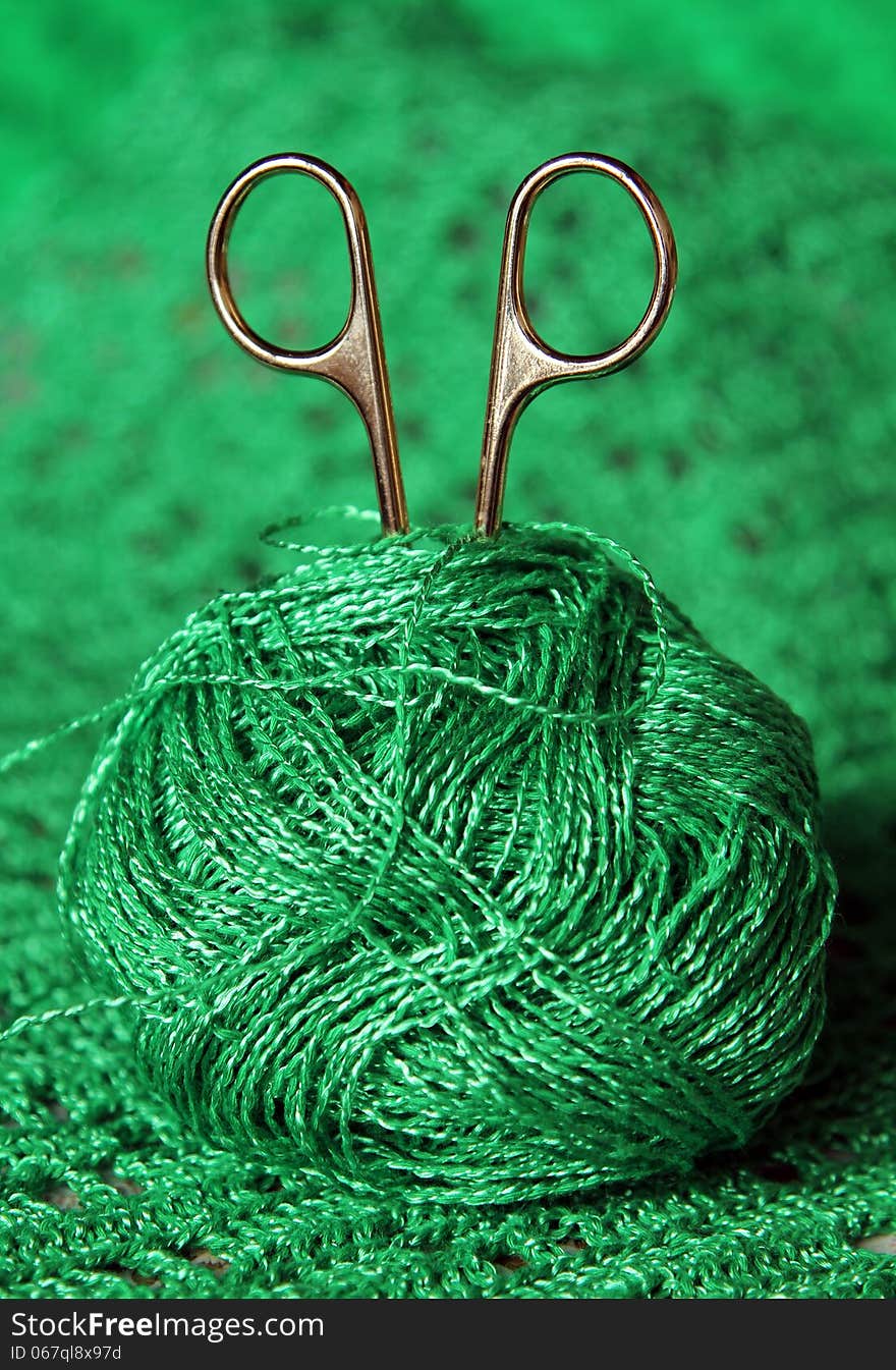 Scissors in a ball of green yarn on a green background