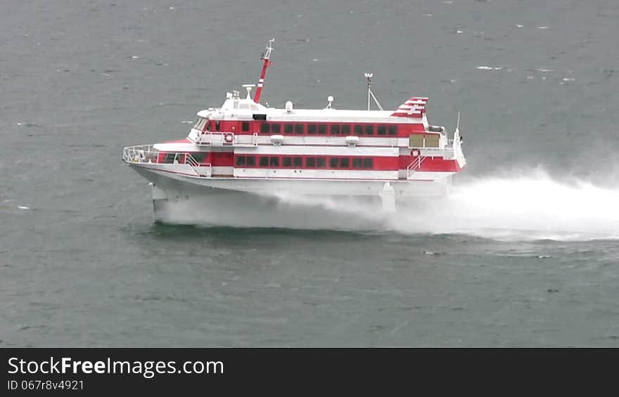 Cloudy weather. On a cold dark sea, swims very fast white boat with red stripes on the hydrofoil. This boat picks up a lot of splashing. Cloudy weather. On a cold dark sea, swims very fast white boat with red stripes on the hydrofoil. This boat picks up a lot of splashing