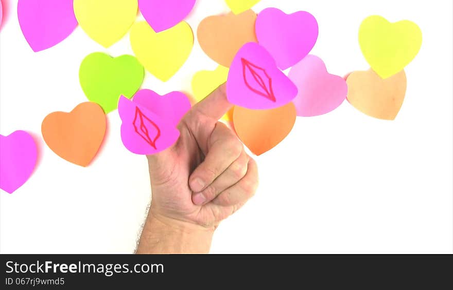 Man's hand with paper labels in the form of hearts on the thumb and forefinger on the background of the lot of labels in the form of hearts. Drawn lips merge in a kiss. Man's hand with paper labels in the form of hearts on the thumb and forefinger on the background of the lot of labels in the form of hearts. Drawn lips merge in a kiss