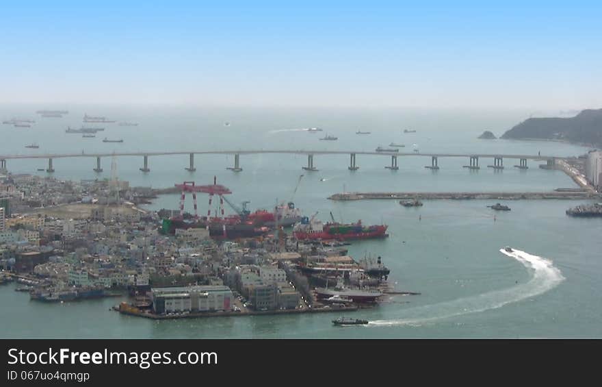 Hot sunny day. Top view of a portion of the port of Pusan. Busy traffic of small boats. On the bridge very quickly passing cars. Many ships are at anchor in the distance. Timelapse. Hot sunny day. Top view of a portion of the port of Pusan. Busy traffic of small boats. On the bridge very quickly passing cars. Many ships are at anchor in the distance. Timelapse