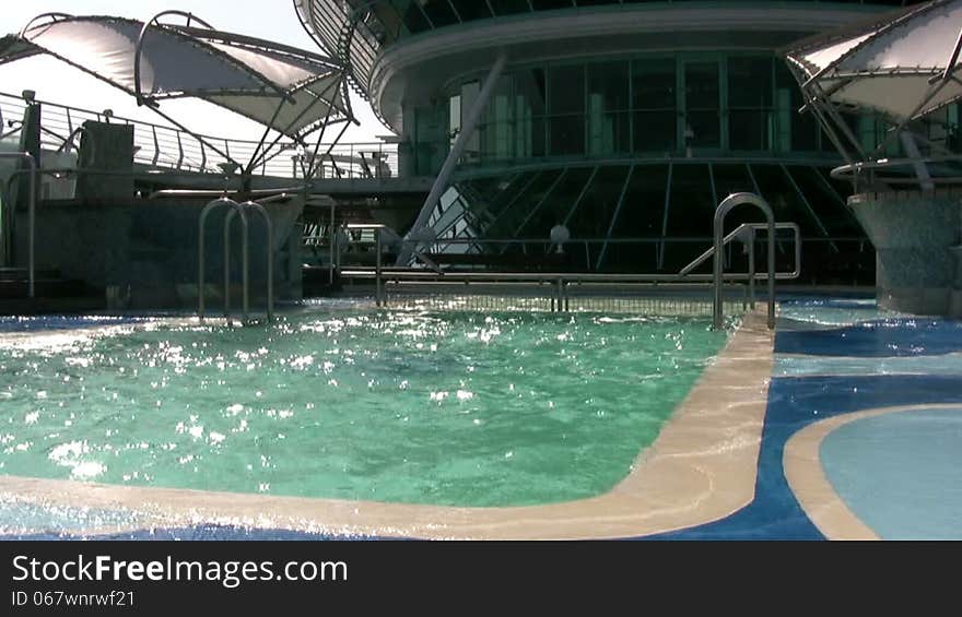 Outdoor swimming pool of large cruise ship during pitching. A bright sunny day. Strong wind. Clean and clear water sparkling in the sun. Outdoor swimming pool of large cruise ship during pitching. A bright sunny day. Strong wind. Clean and clear water sparkling in the sun