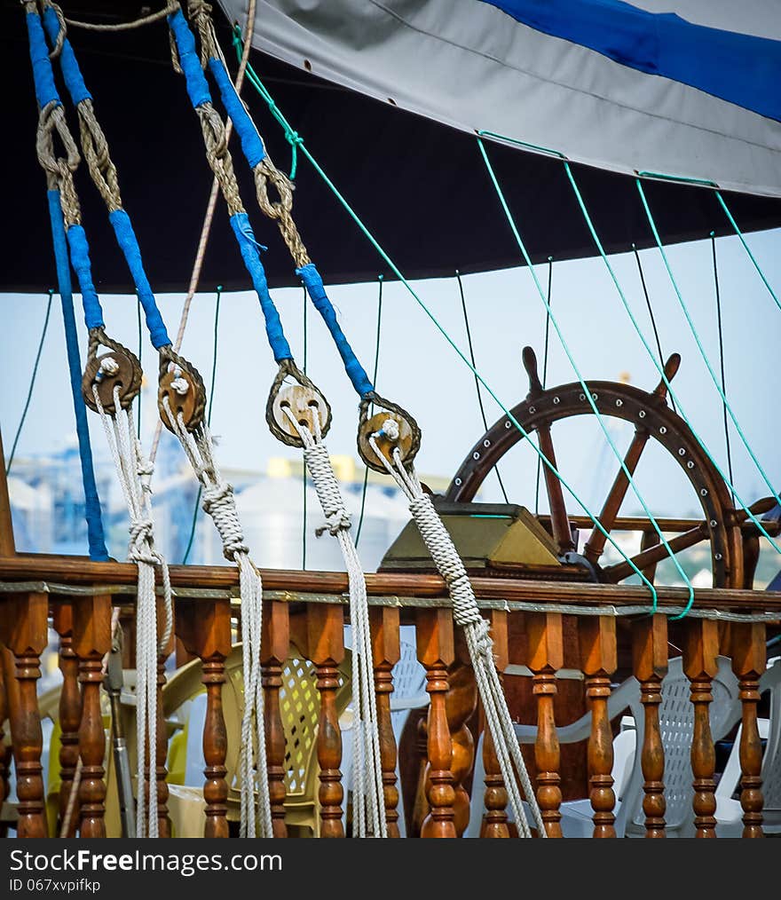 Steering wheel, sea ropes and nautical equipment on wooden yacht. Ship's deck exterior with tackles. Skipper control bridge with captains wheel and navigation tool on the sail vessel. Steering wheel, sea ropes and nautical equipment on wooden yacht. Ship's deck exterior with tackles. Skipper control bridge with captains wheel and navigation tool on the sail vessel.