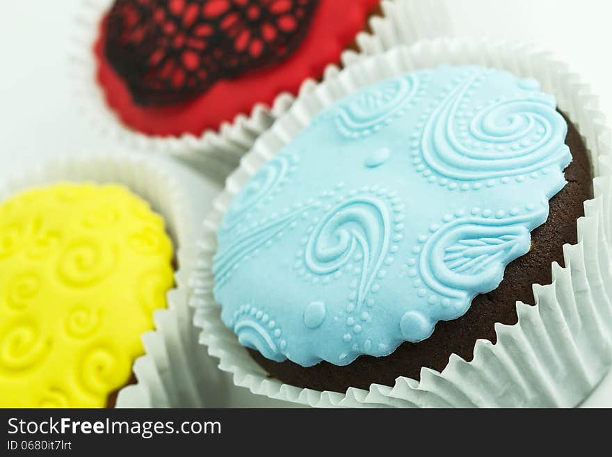 Three cupcakes on the white background. Yellow, blue and red with handmade decoration