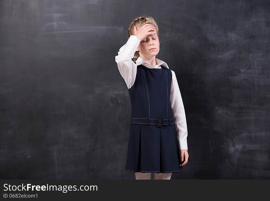 Little schoolgirl with headache holding her head with hands stands at the blackboard. Little schoolgirl with headache holding her head with hands stands at the blackboard