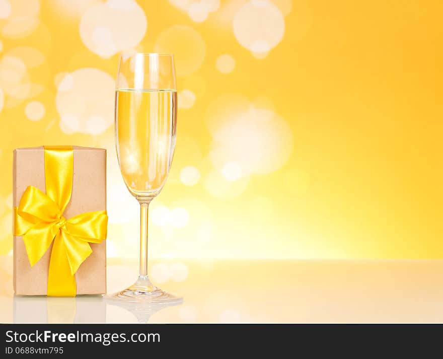 Glass of champagne and gift on an abstract yellow background