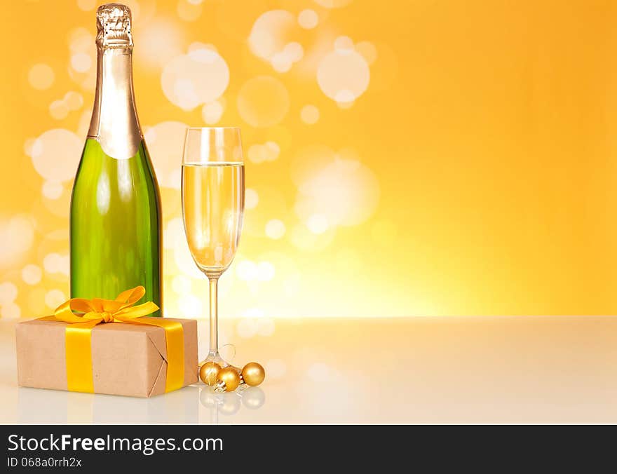 Champagne bottle, glass and gift on an abstract yellow background