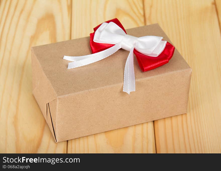 Box from a brown paper with a red-white bow on a wooden surface. Box from a brown paper with a red-white bow on a wooden surface