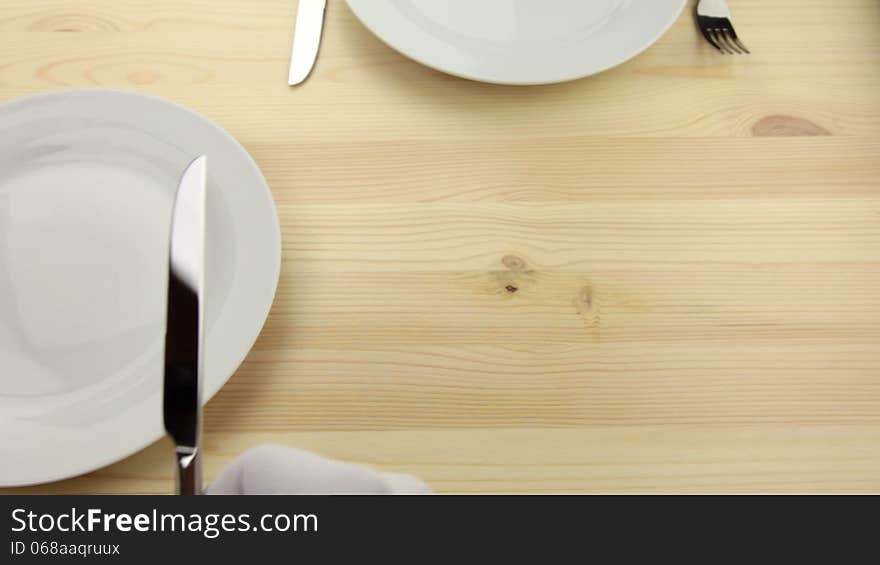 Wooden table. White plates. Hands waiters in white gloves, put a knife and fork. Wooden table. White plates. Hands waiters in white gloves, put a knife and fork