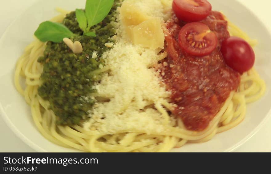 On a white plate rotates pasta. On top of pasta - Pesto, Parmesan and Tomato sauce - in the national colors of the Italian flag. On a white plate rotates pasta. On top of pasta - Pesto, Parmesan and Tomato sauce - in the national colors of the Italian flag