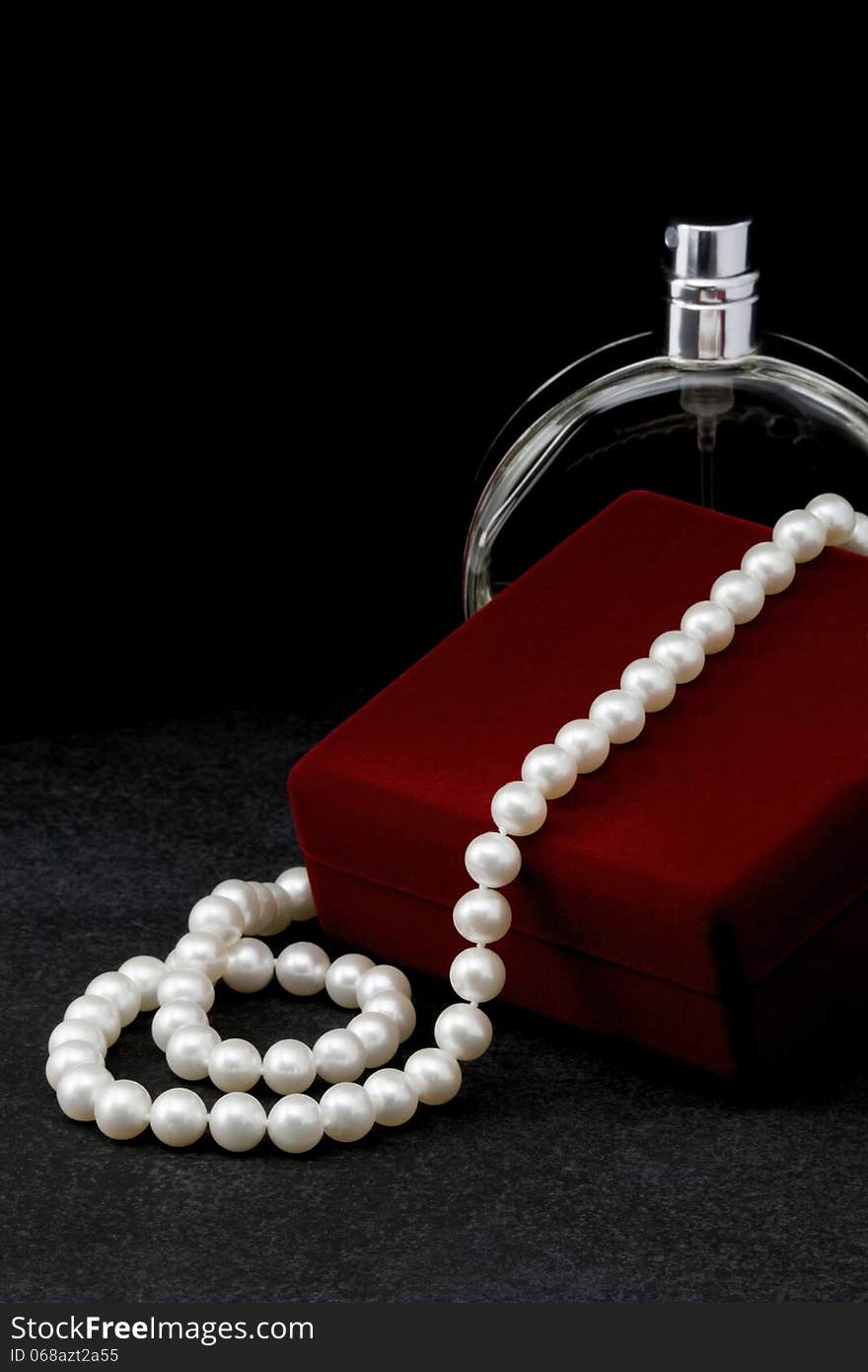 Pearl necklace lies on a red box and a bottle of toilet water