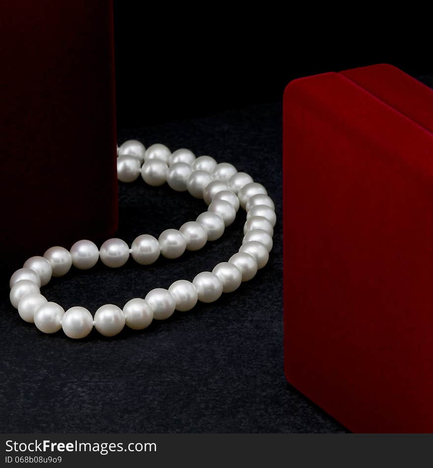 Pearl necklace lies near a red box on a black background.