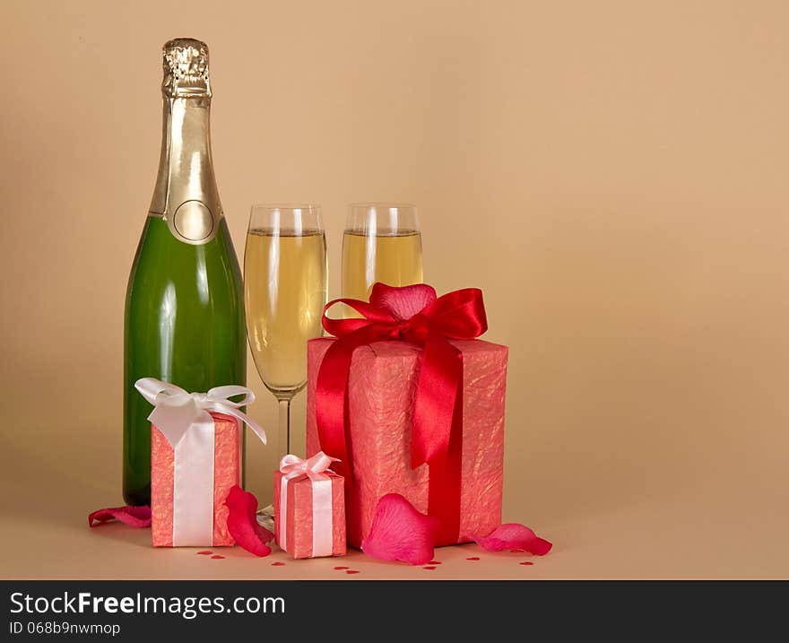 Bottle and wine glasses with champagne, three gift boxes with a ribbon and a bow, rose petals on a beige background