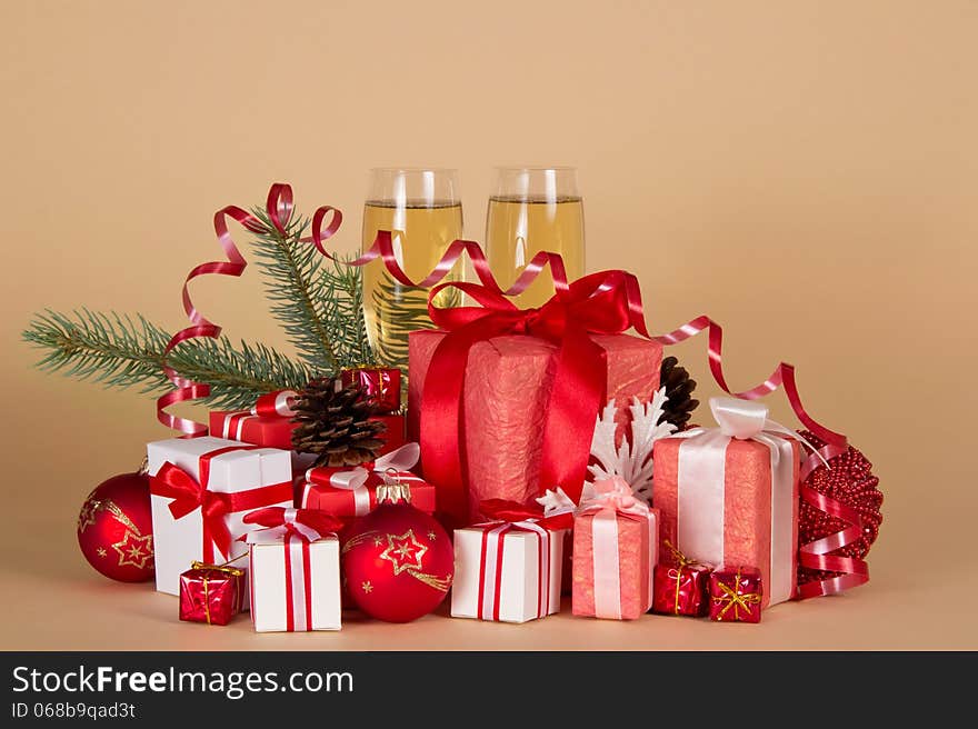 Gift boxes, Christmas toys, pine cones, serpentine and wine glasses with champagne on a beige background