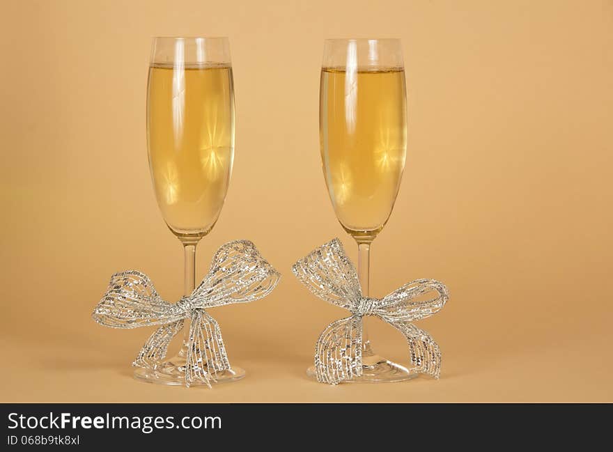 Two glasses with the champagne, decorated silver ribbons on a beige background