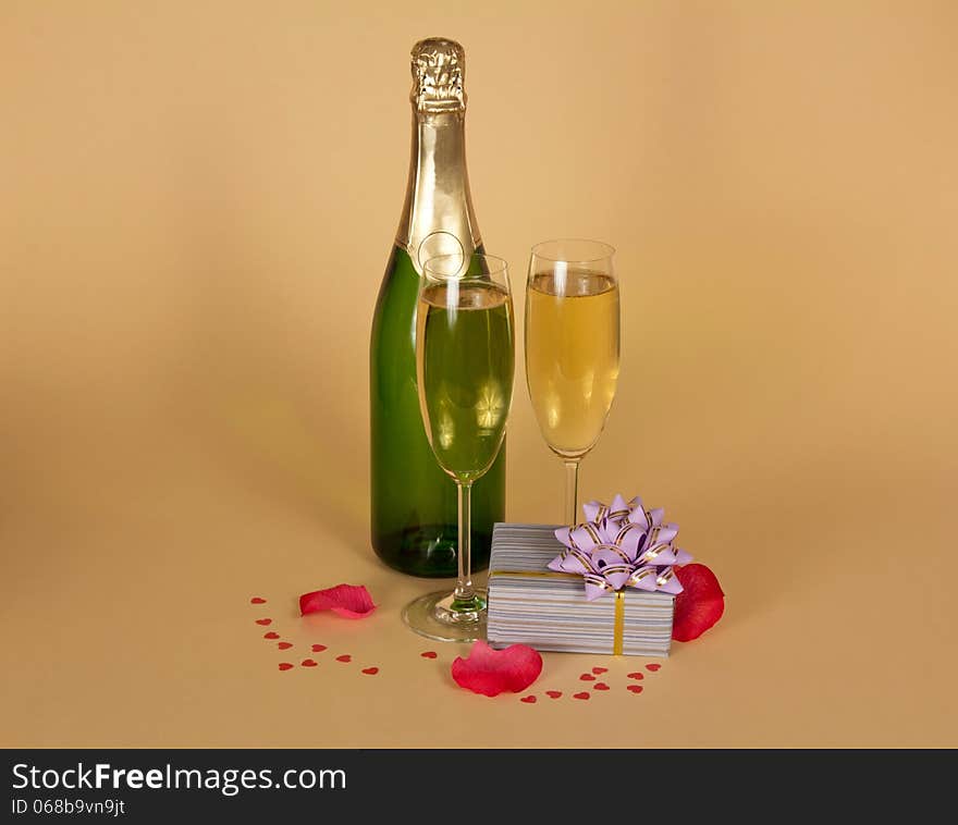 Bottle and two wine glasses of champagne a charming gift box, rose petals and small hearts on a beige background