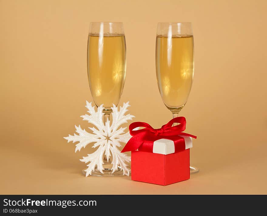 Wine glasses with champagne, a red gift box with a bow and a snowflake on a beige background