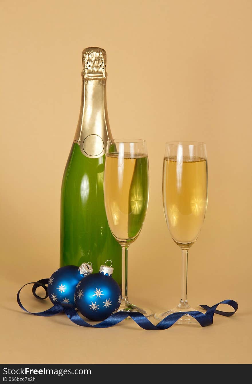 Bottle and wine glasses with champagne, Christmas toys and a serpentine on a beige background. Bottle and wine glasses with champagne, Christmas toys and a serpentine on a beige background