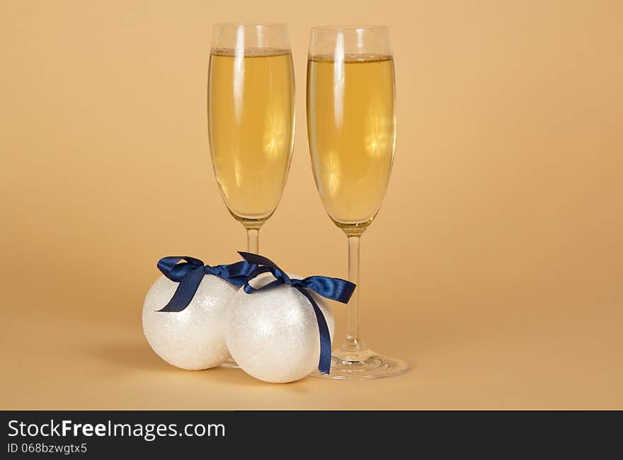 Wine glasses with champagne and New Year's spheres with bows on a beige background. Wine glasses with champagne and New Year's spheres with bows on a beige background.