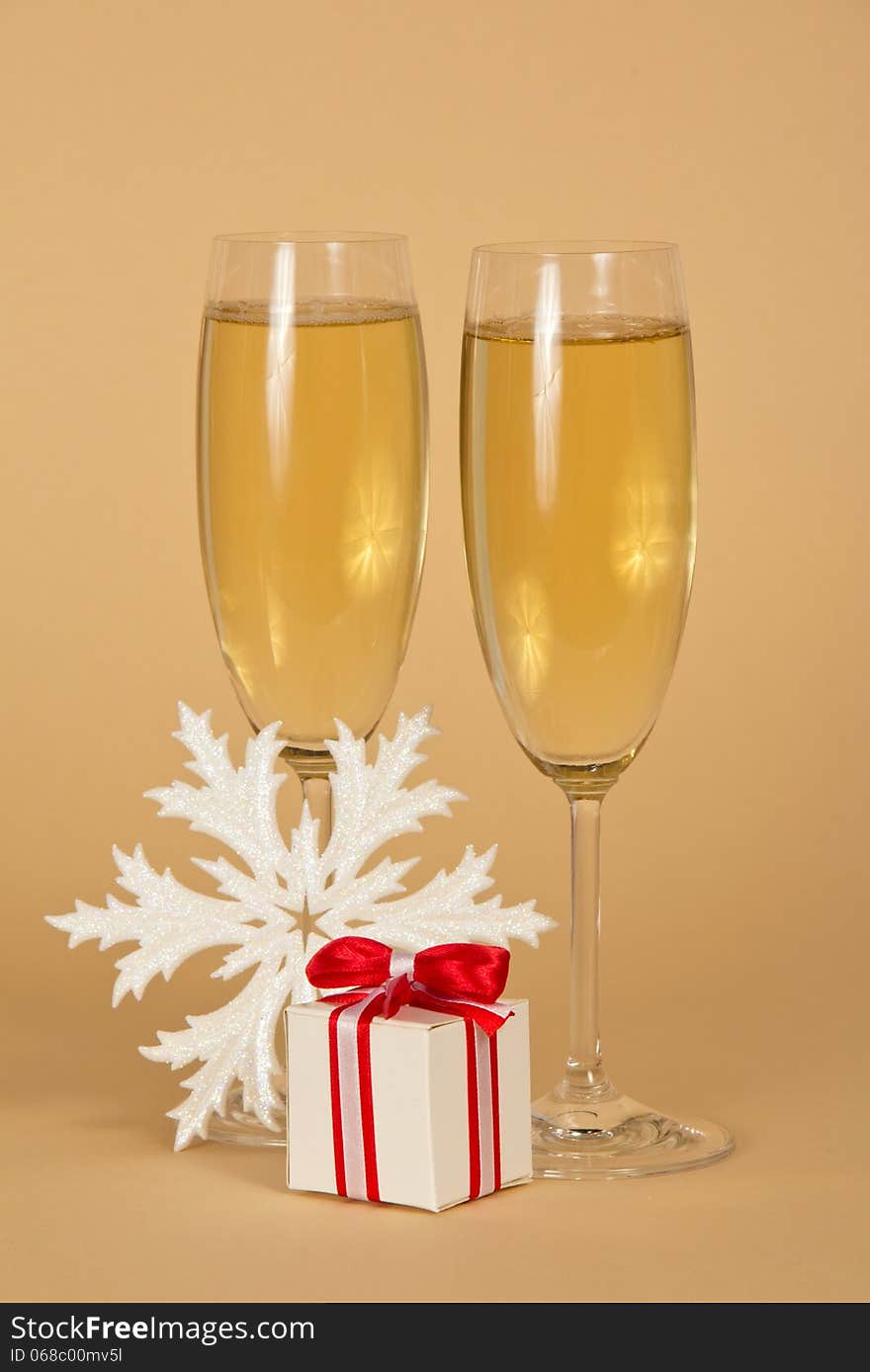 Wine glasses with champagne a beautiful gift box with a bow and snowflake on a beige background