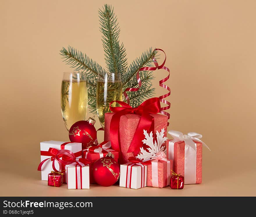 Gift boxes, toys, Christmas tree, serpentine, snowflake and wine glasses with champagne on a beige background