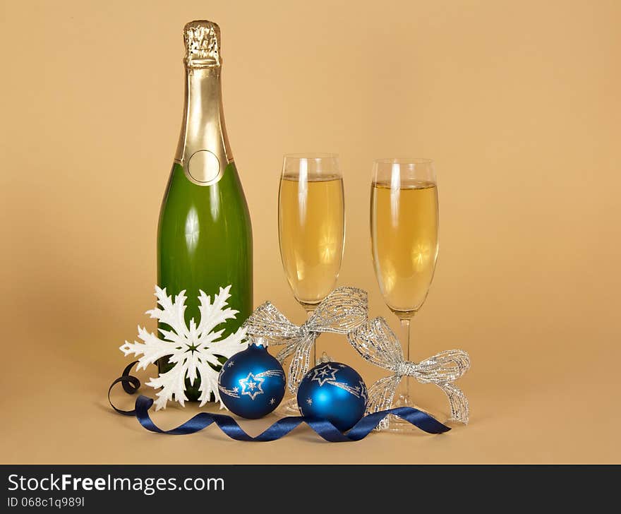 Bottle of champagne, and wine glasses with a silver ribbon, Christmas toys, a snowflake and a serpentine on a beige background. Bottle of champagne, and wine glasses with a silver ribbon, Christmas toys, a snowflake and a serpentine on a beige background
