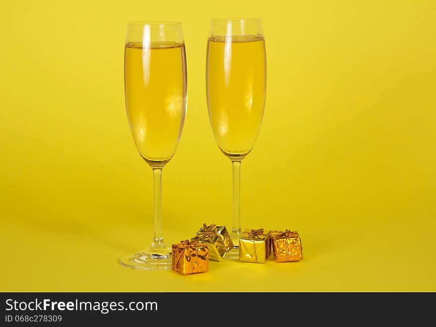 Two wine glasses with champagne and small bright gift boxes on a yellow background