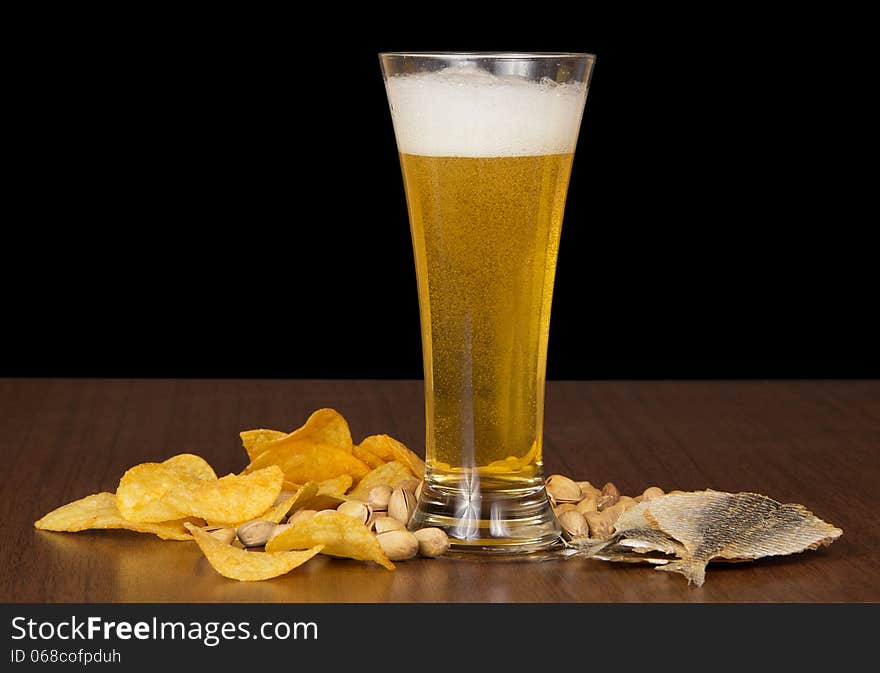 Glass of foamy beer with bubbles, chips, salty fish and the pistachios on the table