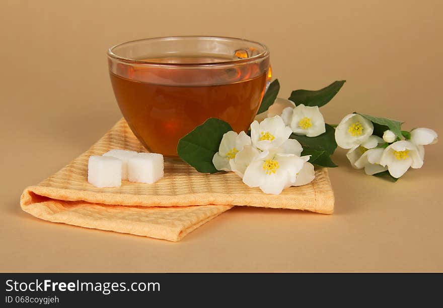 Cup of tea a sugar a branch of a jasmine and a napkin on a beige background. Cup of tea a sugar a branch of a jasmine and a napkin on a beige background