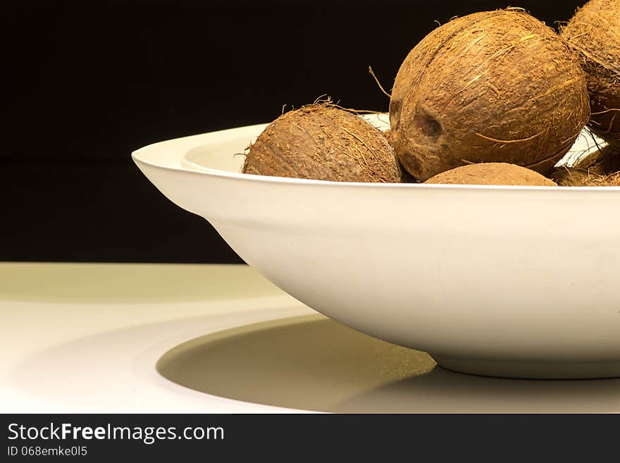 White Bowl of Coconuts on Table with Black Background. White Bowl of Coconuts on Table with Black Background