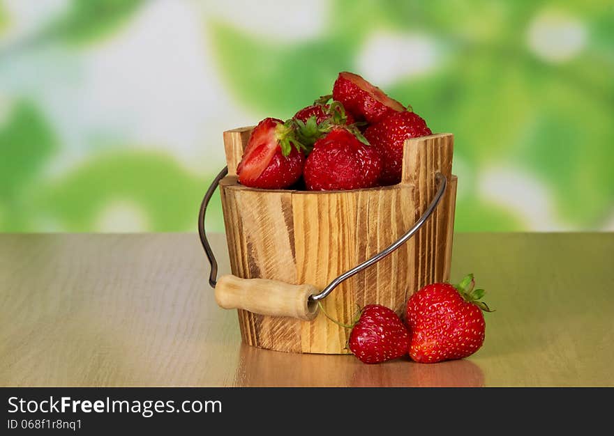 Wooden bucket of ripe fragrant strawberry and two berries near on a table