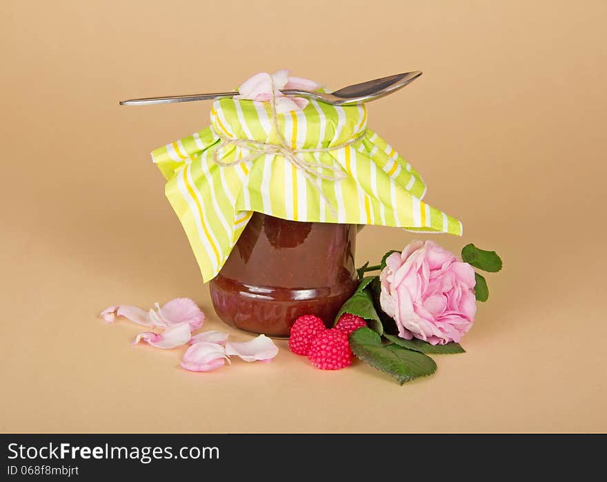 Glass jar with raspberry jam, rose flower on a beige background