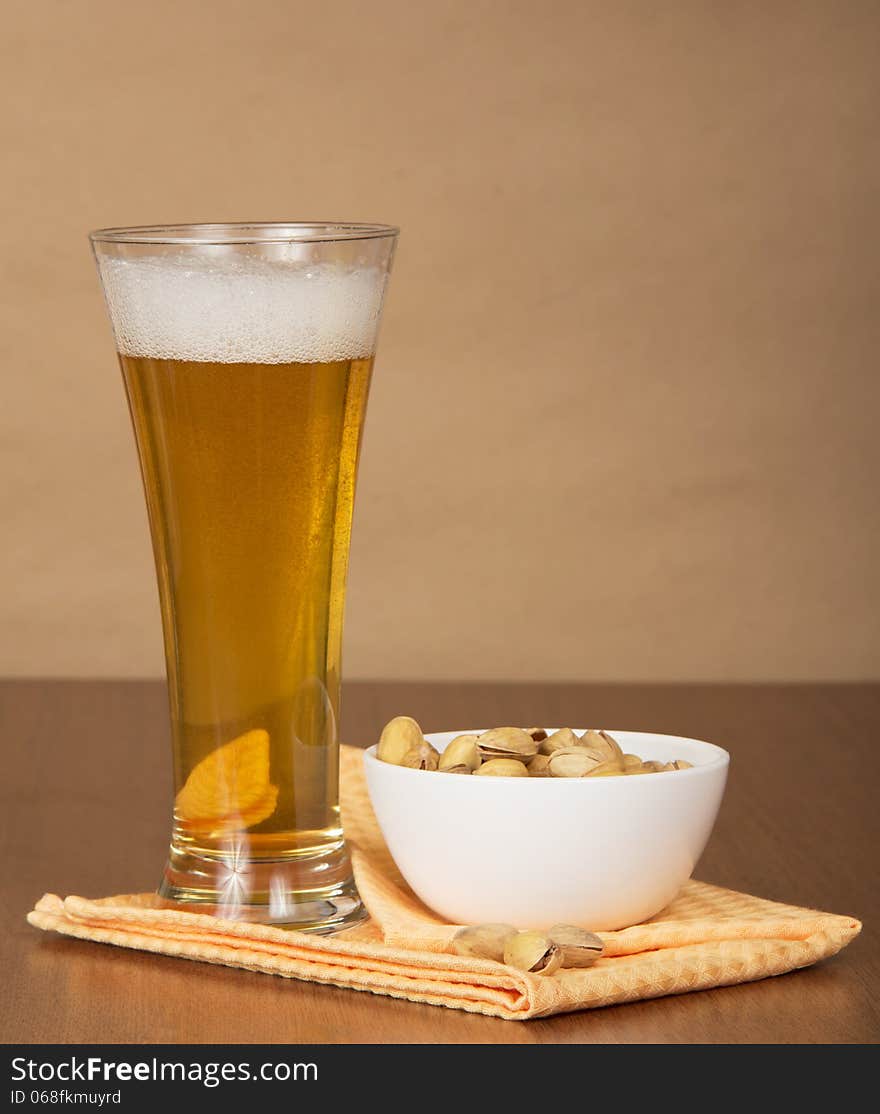 Glass of beer, bowl with pistachios and a napkin against paper. Glass of beer, bowl with pistachios and a napkin against paper