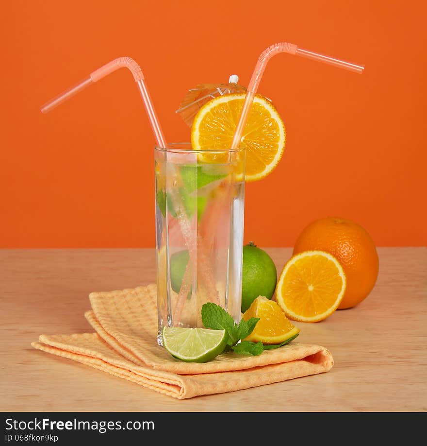 The drink glass with a straw, is decorated with an umbrella and an orange segment, a citrus and a napkin on a table