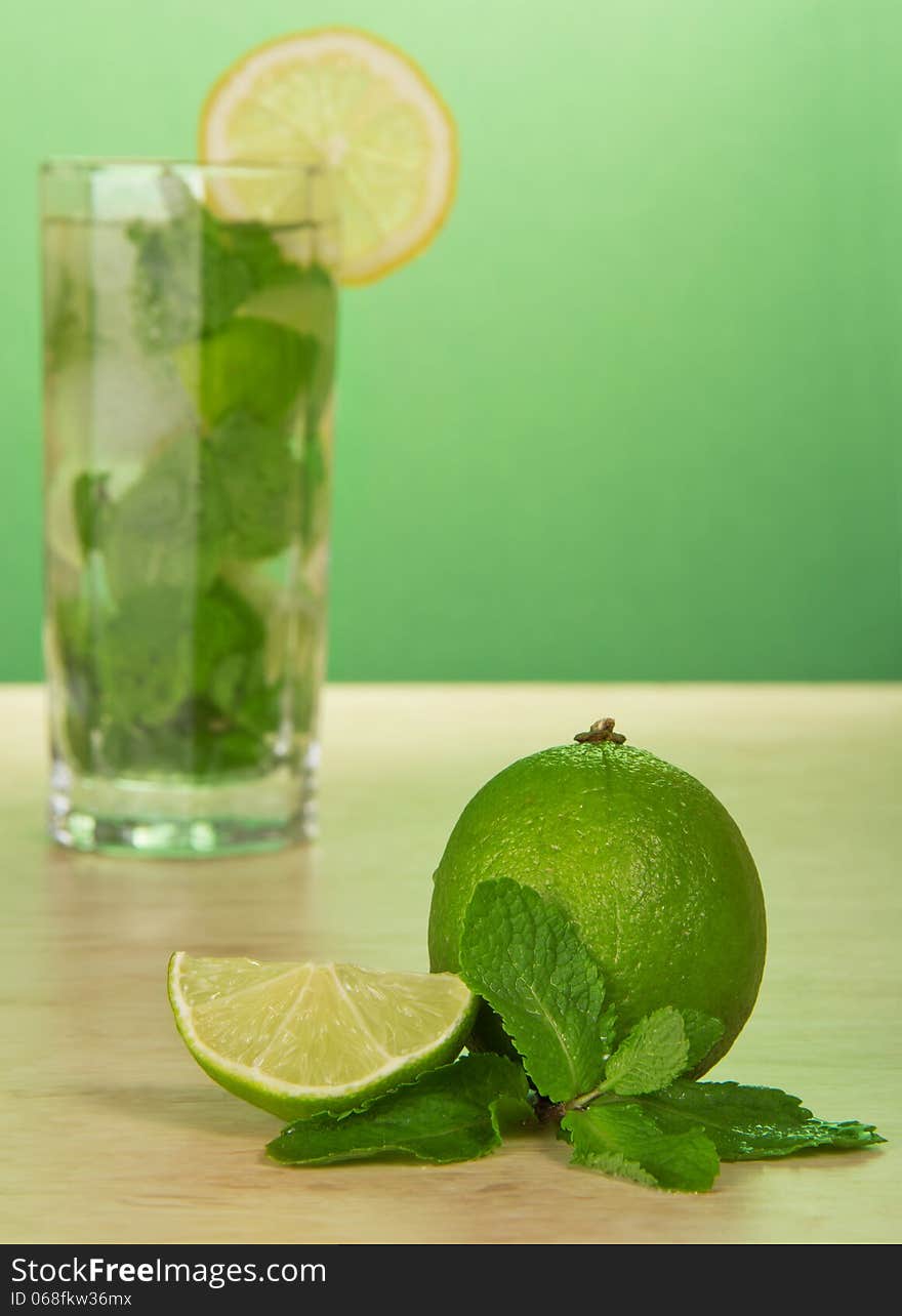 Mojito cocktail, slice of a lemon, and spearmint leaves, on a green background