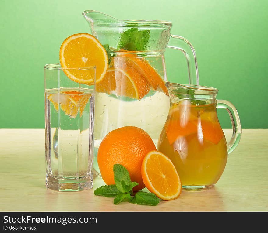 Jugs with drinks and a glass, oranges and spearmint on a table. Jugs with drinks and a glass, oranges and spearmint on a table