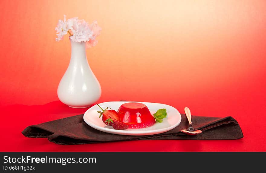 Plate with jelly, a spoon, a vase with the flowers and a brown; napkin on a pink background. Plate with jelly, a spoon, a vase with the flowers and a brown; napkin on a pink background