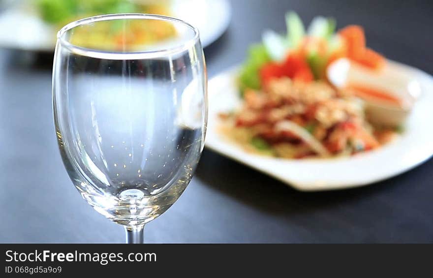 Pouring drinking water into wine glass with food in background