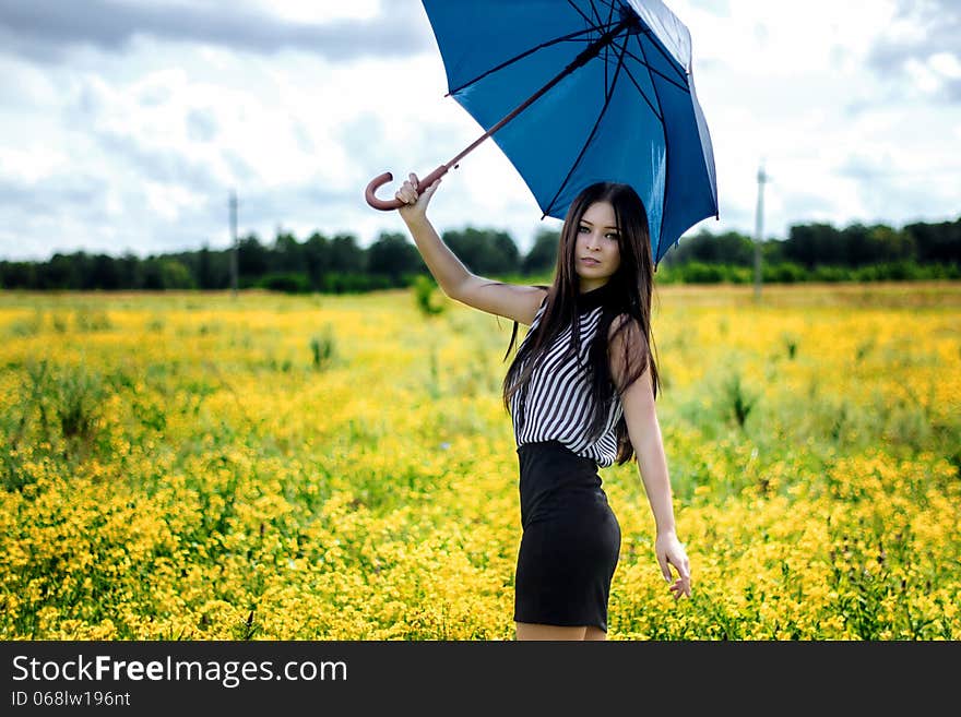 Slim girl standing with blue umbrella in yellow flowers field