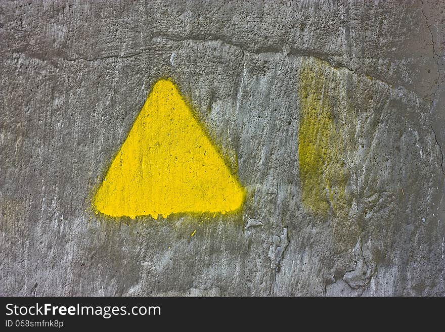 Texture of concrete gray wall with yellow triangle painted on it